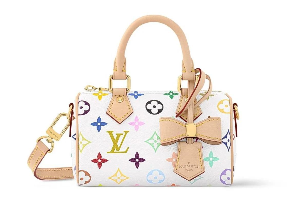 A small white barrel shaped bag printed with a multicoloured monogram pattern, natural leather handles, a bow at the front and a detachable strap.