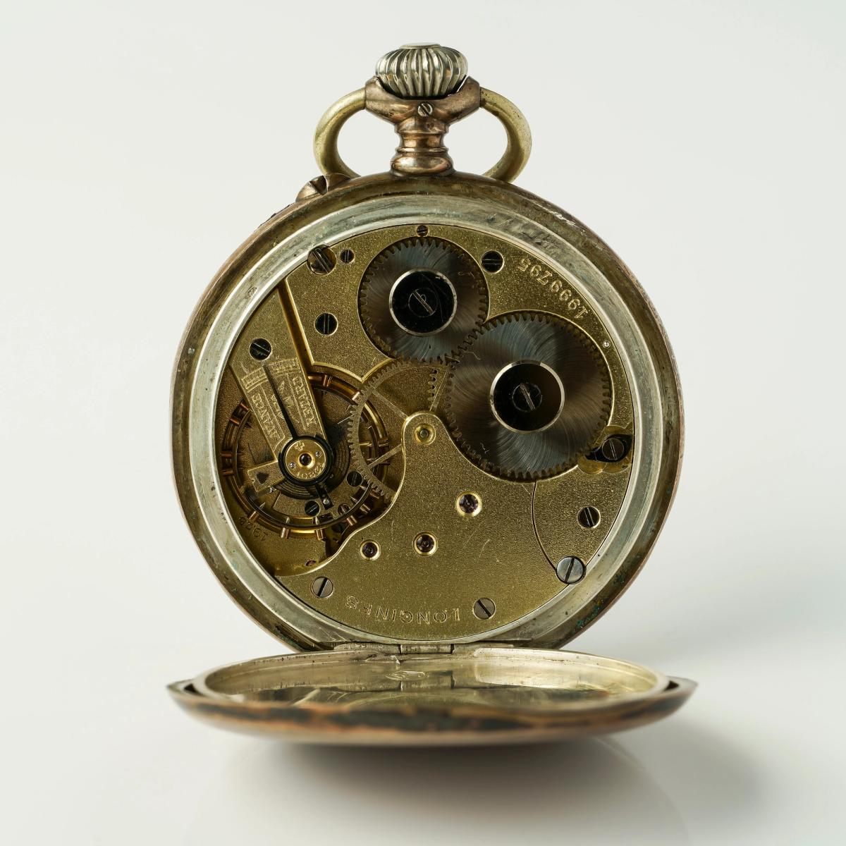 A silver pocket watch photographed on white with its hinged back swung open, the full gilt movement exposed and a serial number legible on the plate.