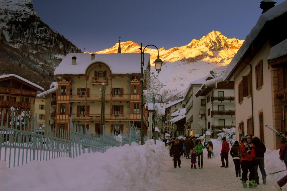 A mountain valley in Alagna Valsesia beneath Monte Rosa, with a walking path between stone and timber houses.
