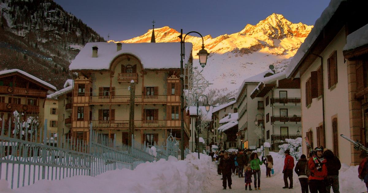 A mountain valley in Alagna Valsesia beneath Monte Rosa, with a walking path between stone and timber houses.