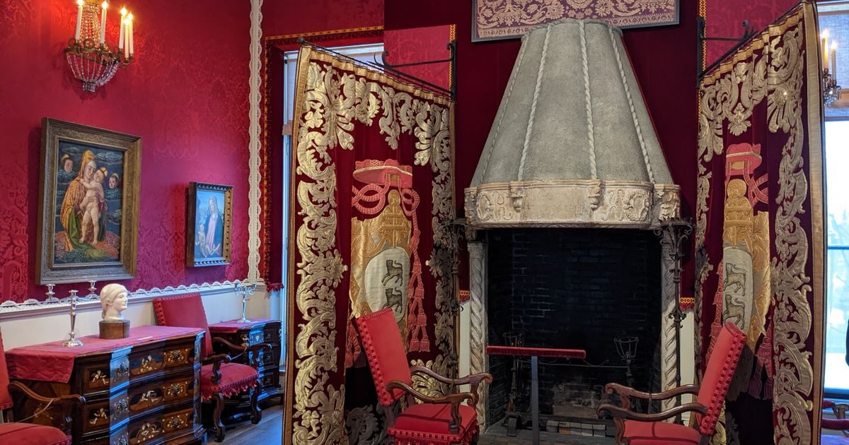 An interior gallery at the Isabella Stewart Gardner Museum, hung densely with paintings and tapestries above patterned walls and antique furniture, arranged as a domestic room rather than a modern gallery.