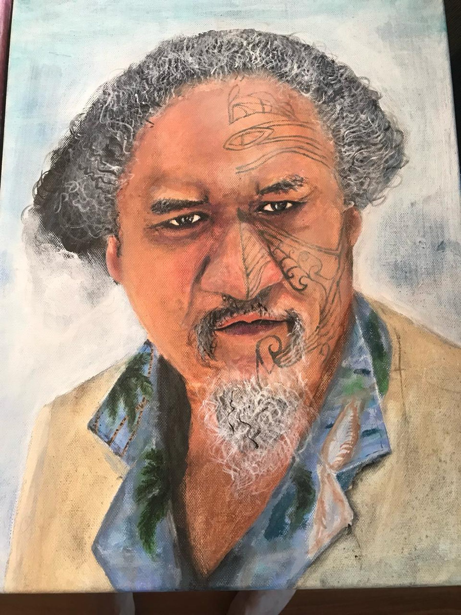 A portrait painting of a man with greying hair, facial hair, and moko-inspired linework across the face, wearing a light jacket over a blue shirt.