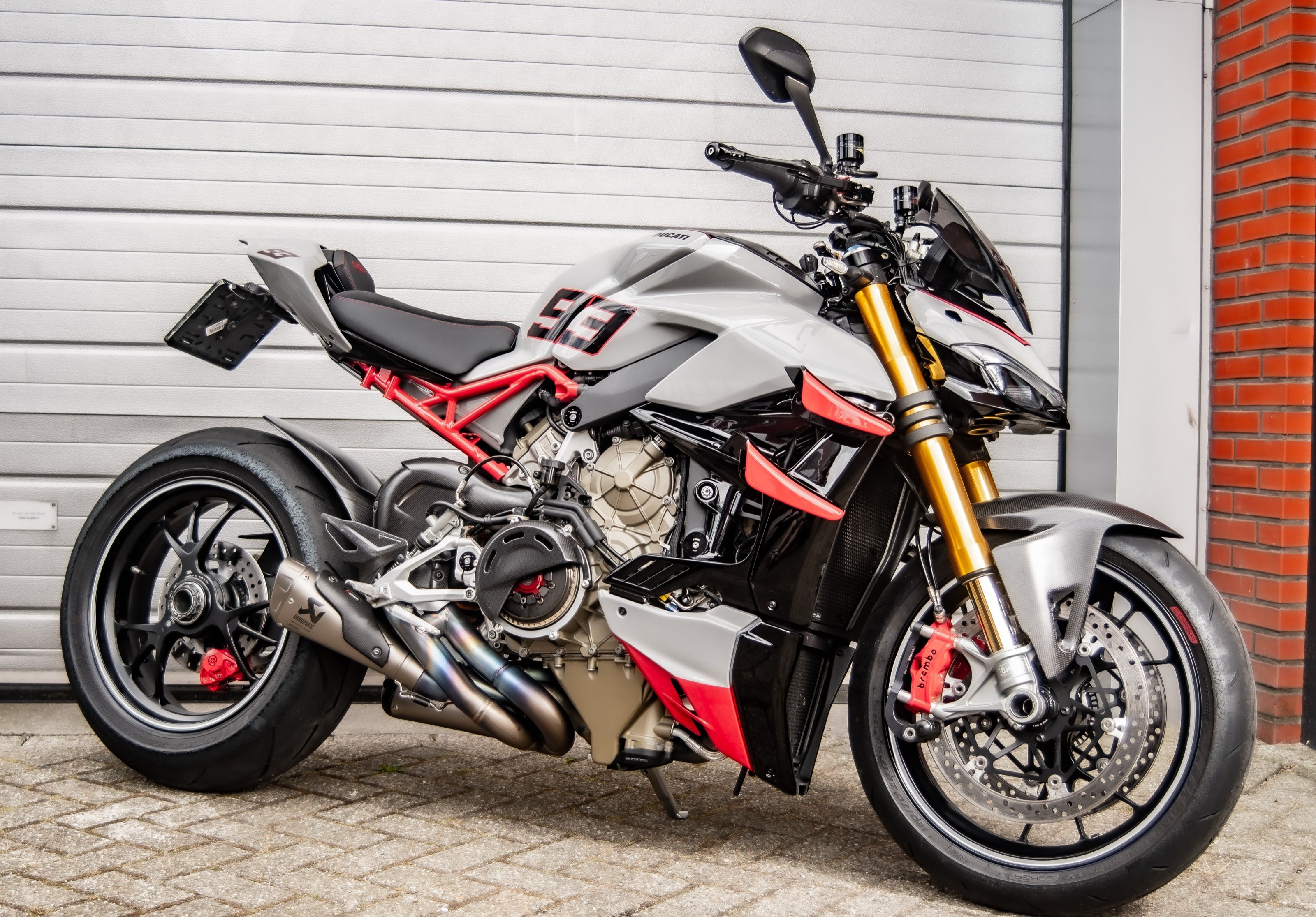 Ducati Streetfighter V4S in lichtgrijs en rood voor een garagedeur