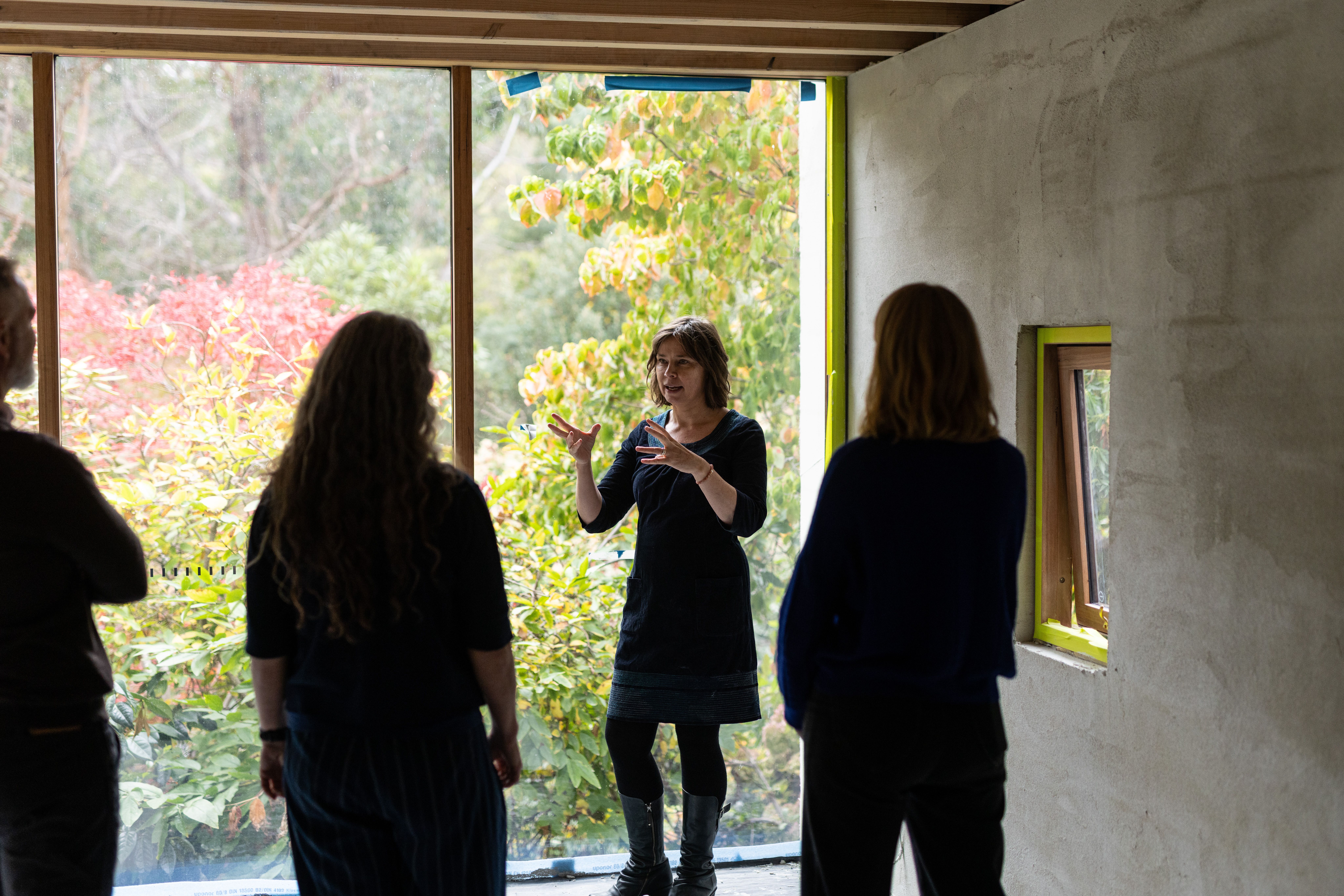 a white woman with short brown hair stands gesticulates to 3 people with their backs to the camera in front of a window that looks out to a garden | Tempo Therapy and Consulting | therapy and supervision in healthcare