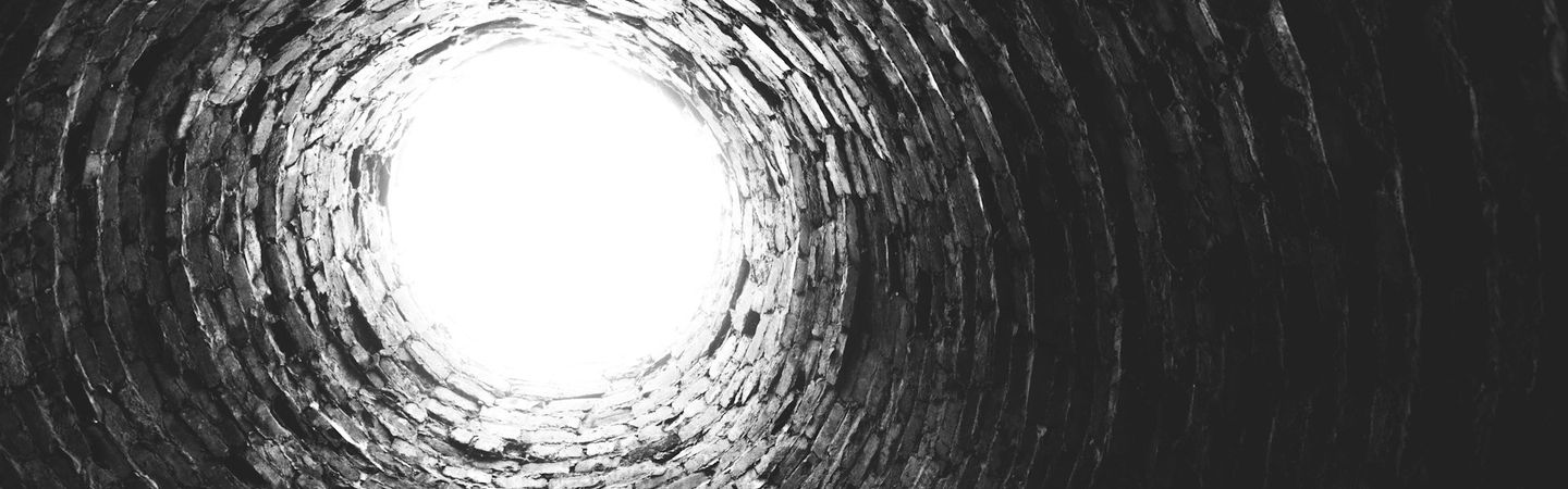 a black and white photo looking up from the bottom of a dark brick tunnel that opens into a circle of light | Tempo Therapy and Consulting | moving out despair in healthcare