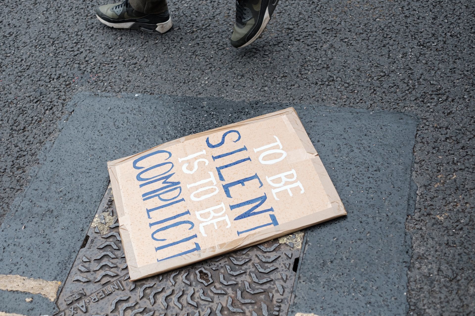 a placard lies on the street with the words 'to be silent is to be complicit' | near and far enemies of fierce compassion | tempo therapy and consulting