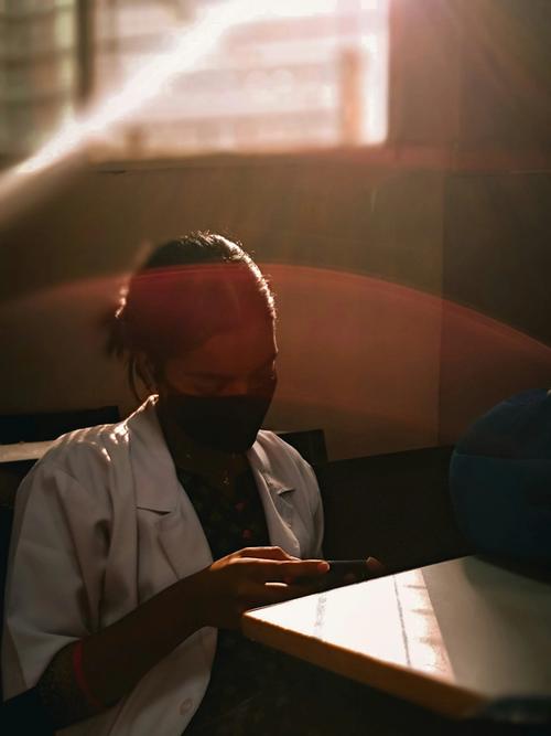 A brown-skinned female clinician sits at a desk in a white coat with the sun shining through | Tempo Therapy and Consulting | dual focus in healthcare work