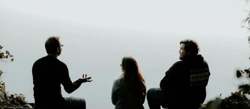 two men and a woman sit in discussion in the foreground with their backs to the camera, with leaves and branches at the sides | Therapeutic supervision | Tempo Therapy and Consulting