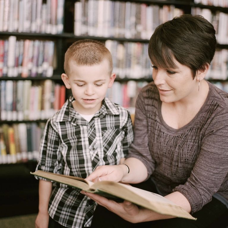 Woman teaching young child with a book in library