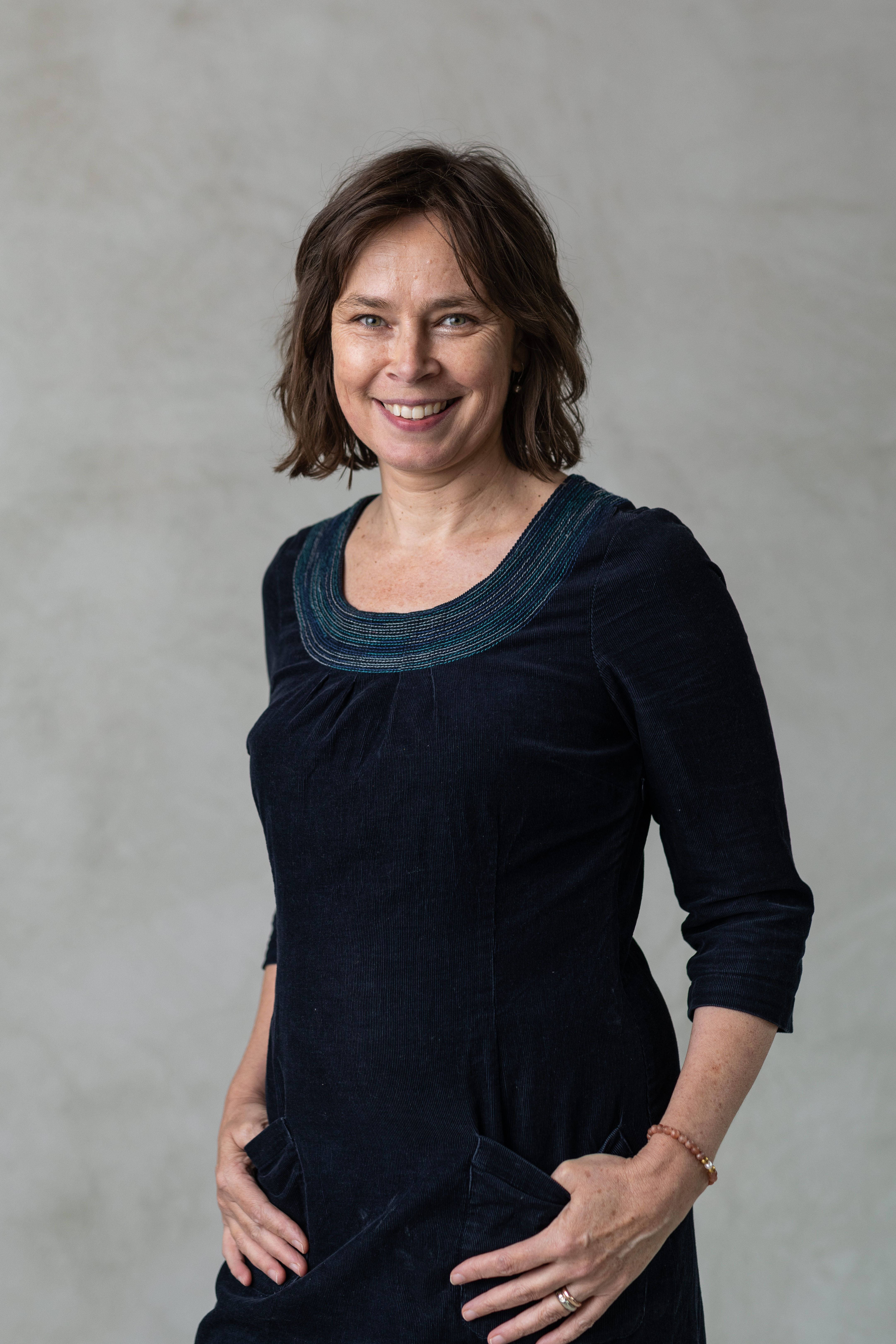 a smiling white woman with short brown hair stands in front of a grey wall | Tempo Therapy and Consulting | therapy and supervision in healthcare