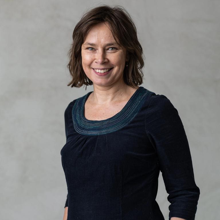 a smiling white woman with short brown hair stands in front of a grey wall | Tempo Therapy and Consulting | therapy and supervision in healthcare