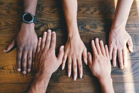 5 hands with varying shades of brown and white skin lay flat on a wooden desk | group supervision | Tempo Therapy and Consulting