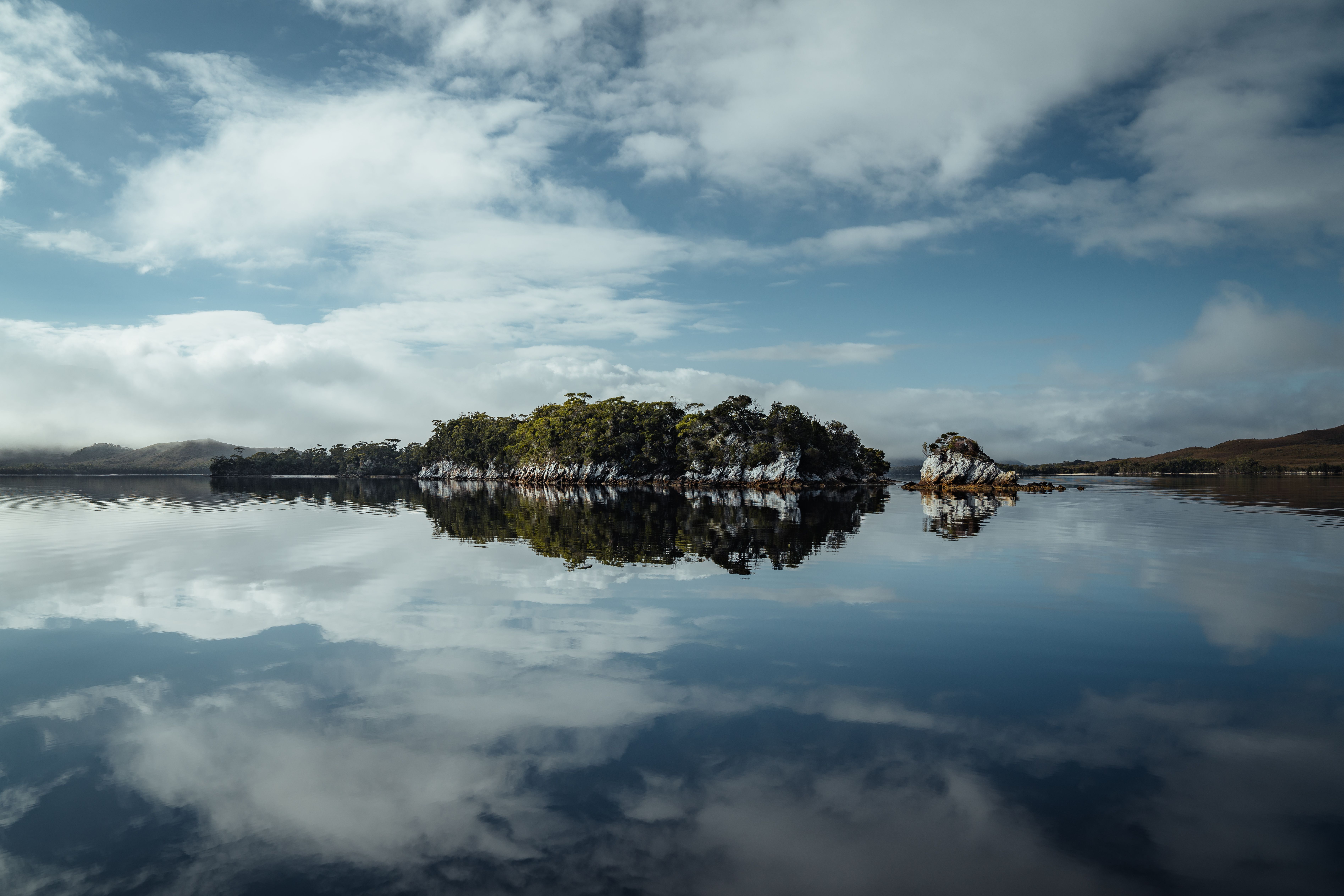 Small island with trees reflected in calm water under a soft pink and blue sky. | how to leave clinical work at work | Tempo Therapy and Consulting