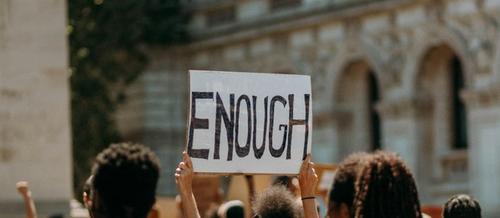 A group of people hold up a sign saying 'ENOUGH' on a street | anti-self care revolution | Tempo Therapy and Consulting