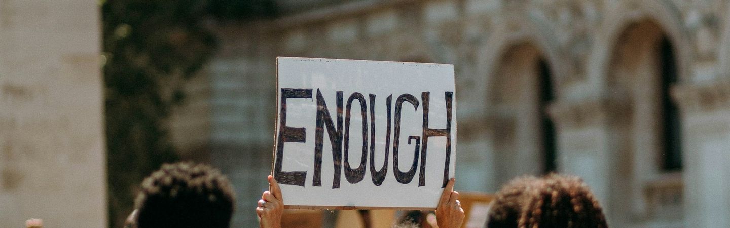 A group of people hold up a sign saying 'ENOUGH' on a street | anti-self care revolution | Tempo Therapy and Consulting