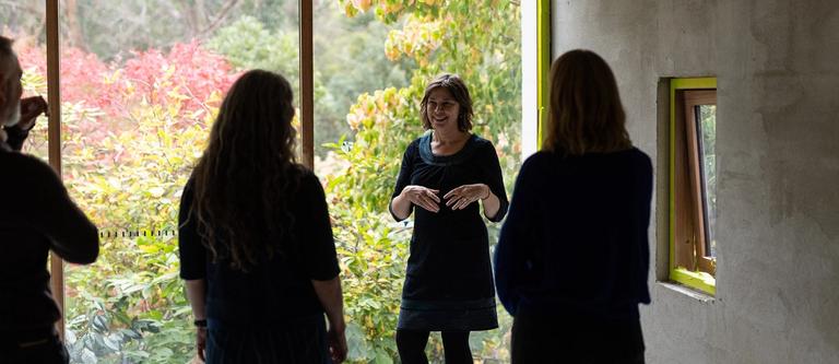 a woman with short brain hair stands in front of a large window with three people in the foreground | clearing the lens for therapists and clinicians | Tempo Therapy and Consulting