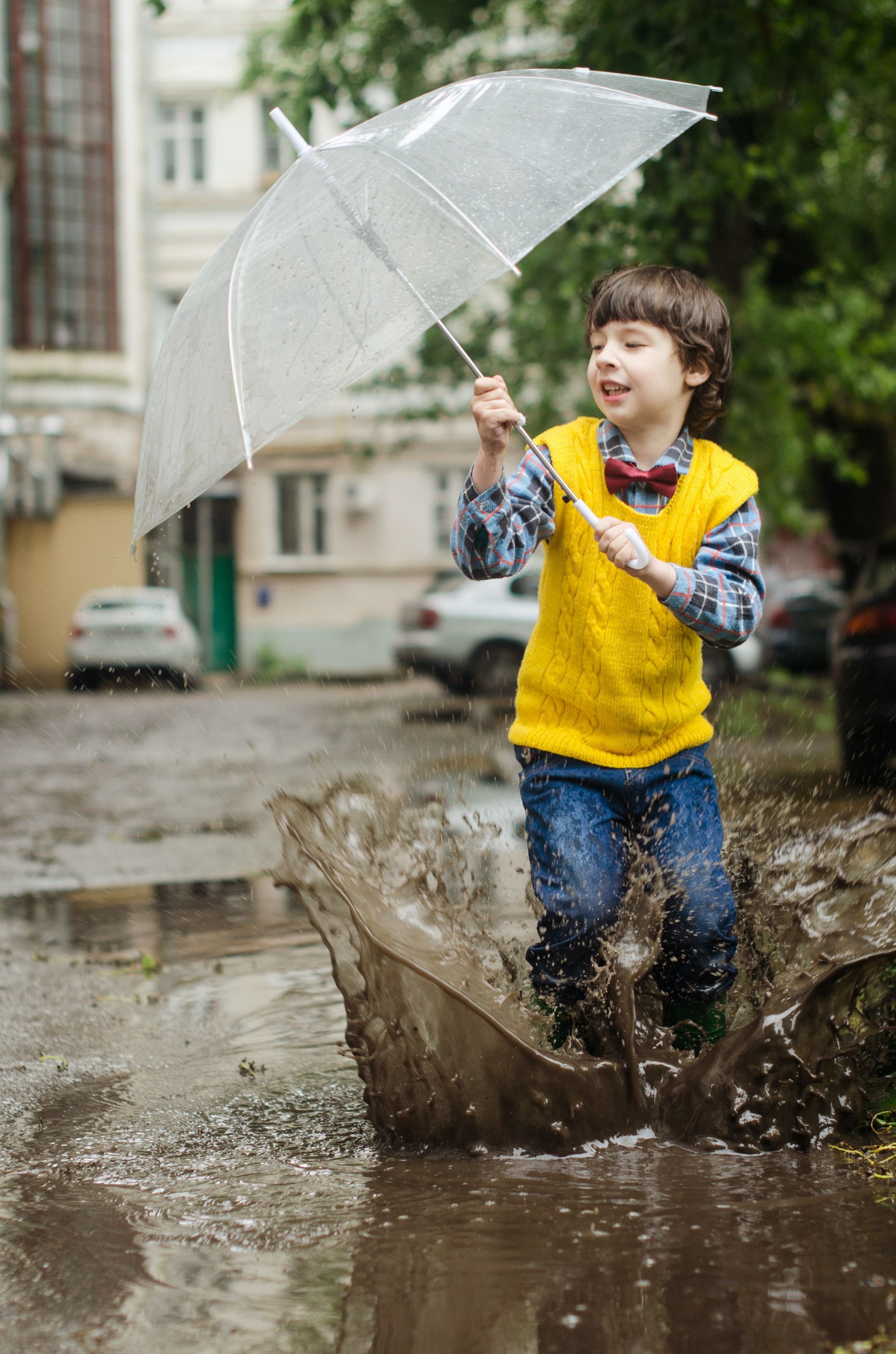child splashing in muddy puddle with umbrella