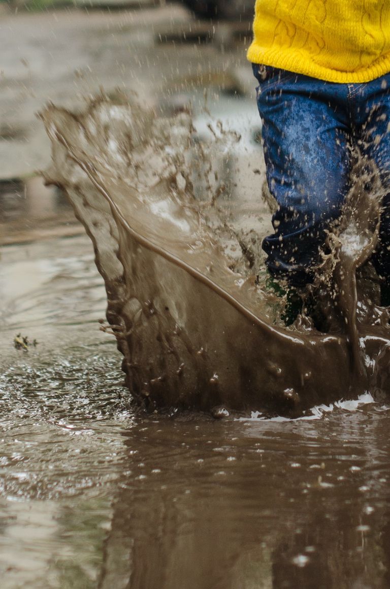 child splashing in muddy puddle with umbrella