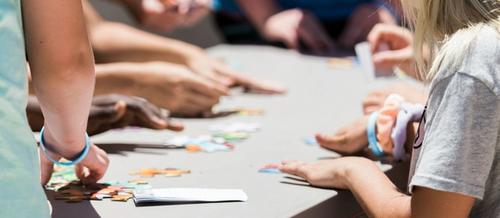 5 hands with varying shades of brown and white skin lay flat on a wooden desk | group supervision | Tempo Therapy and Consulting