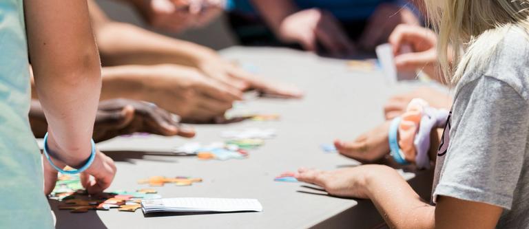 5 hands with varying shades of brown and white skin lay flat on a wooden desk | group supervision | Tempo Therapy and Consulting