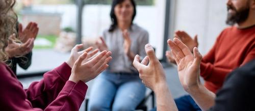 A group of adults sit in a circle, hands in the foreground are raised to clap | Group supervision | Tempo Therapy and Consulting