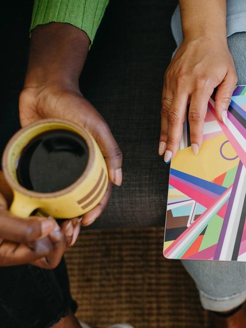 aerial view of a white-skinned person holding a colourful iMac in their lap and a black-skinned person holding a yellow cup of coffee | group supervision | Tempo Therapy and Consulting