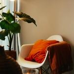 a cosy room corner with a white chair and orange cushion is lit by a warm lamp | therapy for therapists, clinicians and service leaders | Tempo Therapy and Consulting