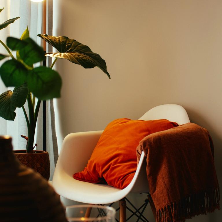 a cosy room corner with a white chair and orange cushion is lit by a warm lamp | therapy for therapists, clinicians and service leaders | Tempo Therapy and Consulting
