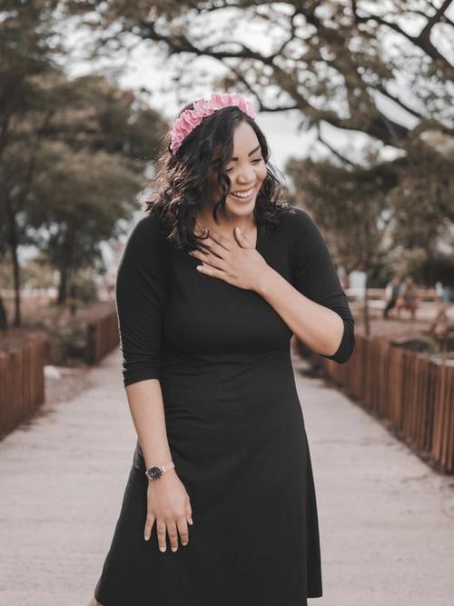 A woman with brown skin stands in a park laughing with one hand open on her chest | Tempo Therapy and Consulting | kindness for healthcare workers