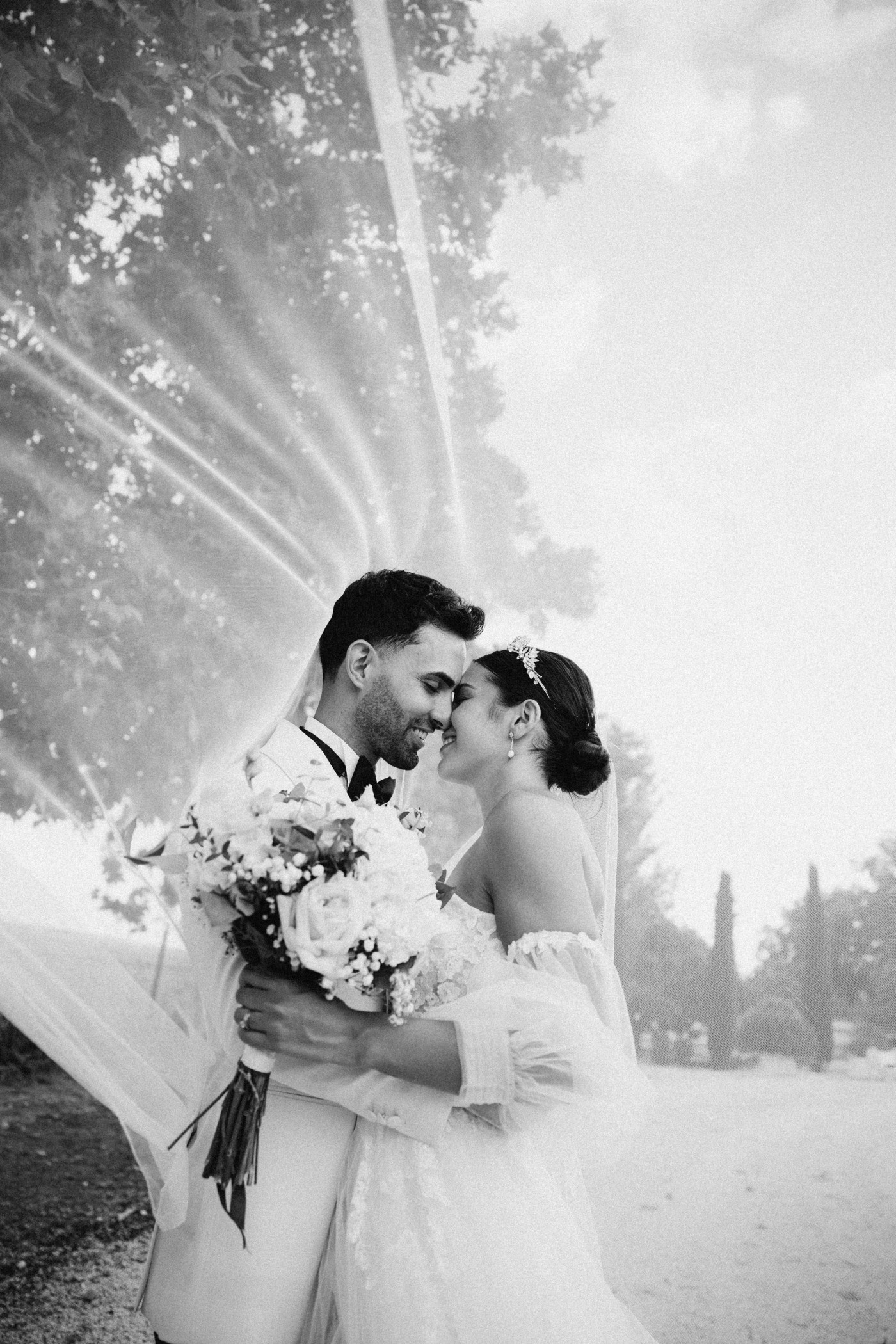 The bride's veil wrapping the couple against the light, in black and white