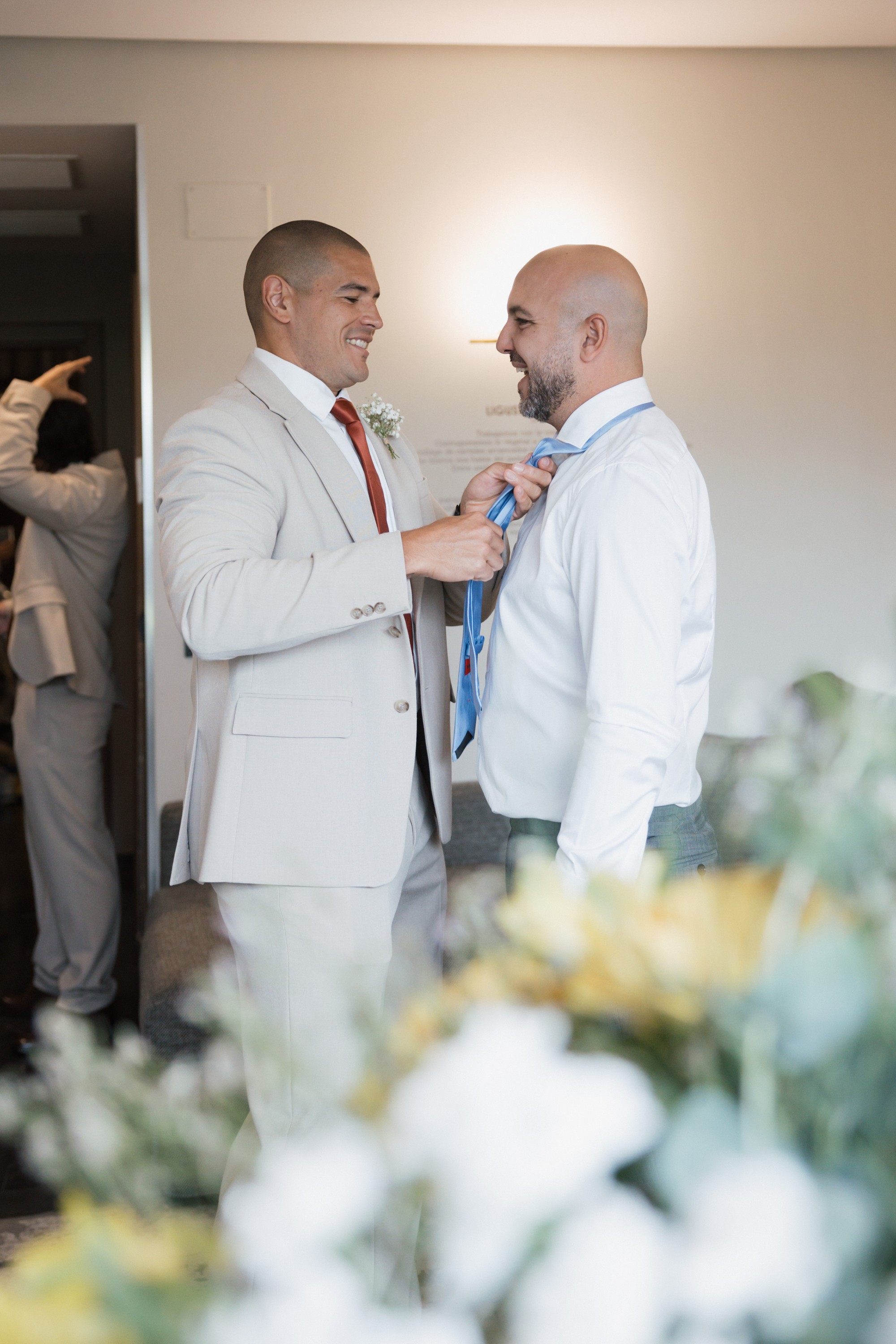 Un amigo le ajusta la corbata azul al novio entre risas durante los preparativos