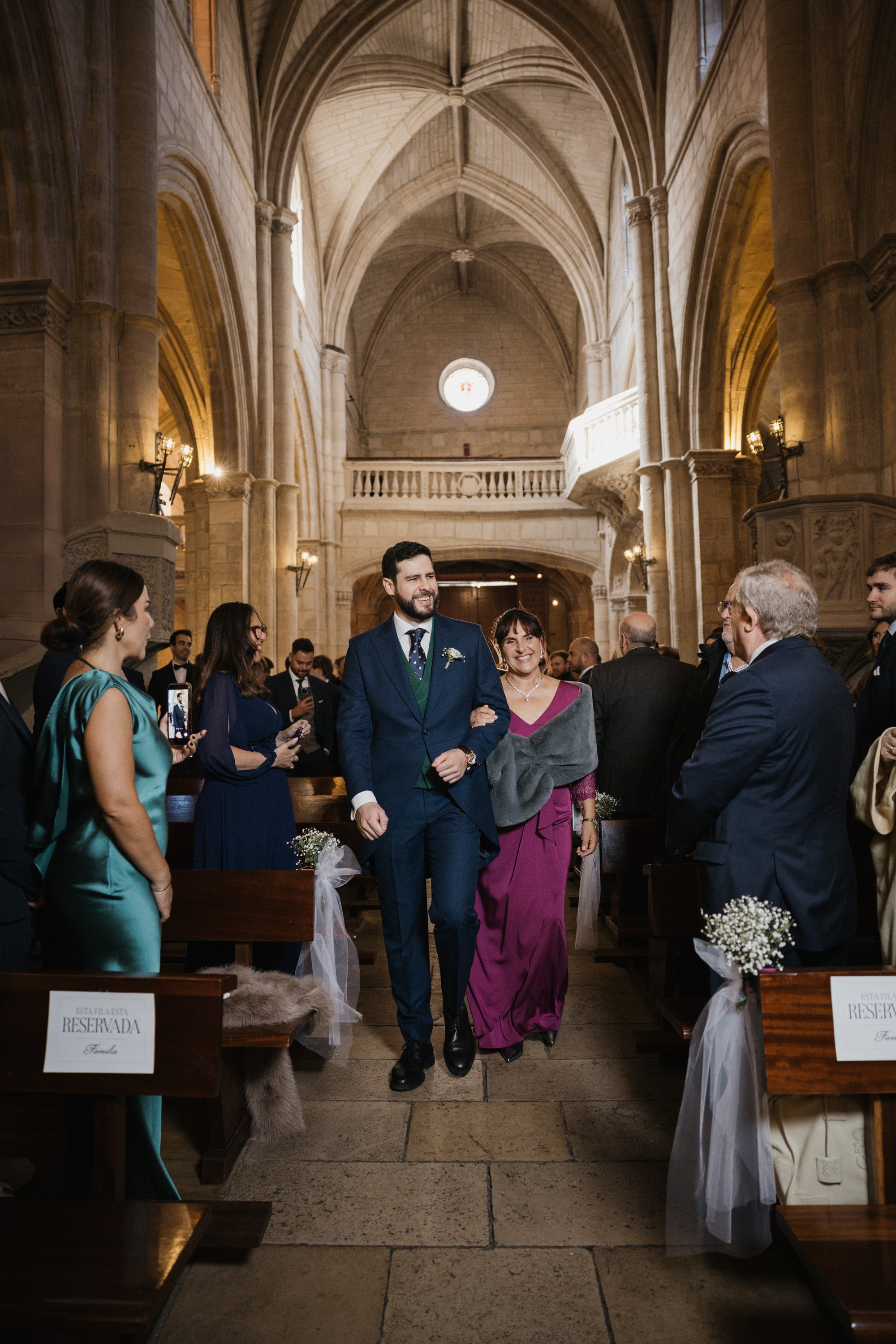 El novio recorre la nave de la iglesia del brazo de una invitada entre los bancos reservados