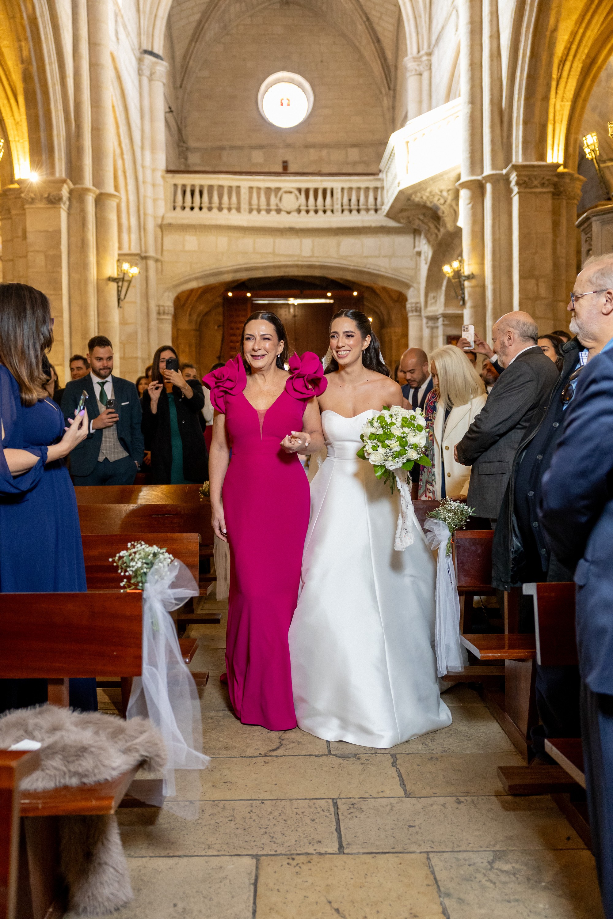 La novia entra en la iglesia del brazo de una invitada mientras todos la fotografían