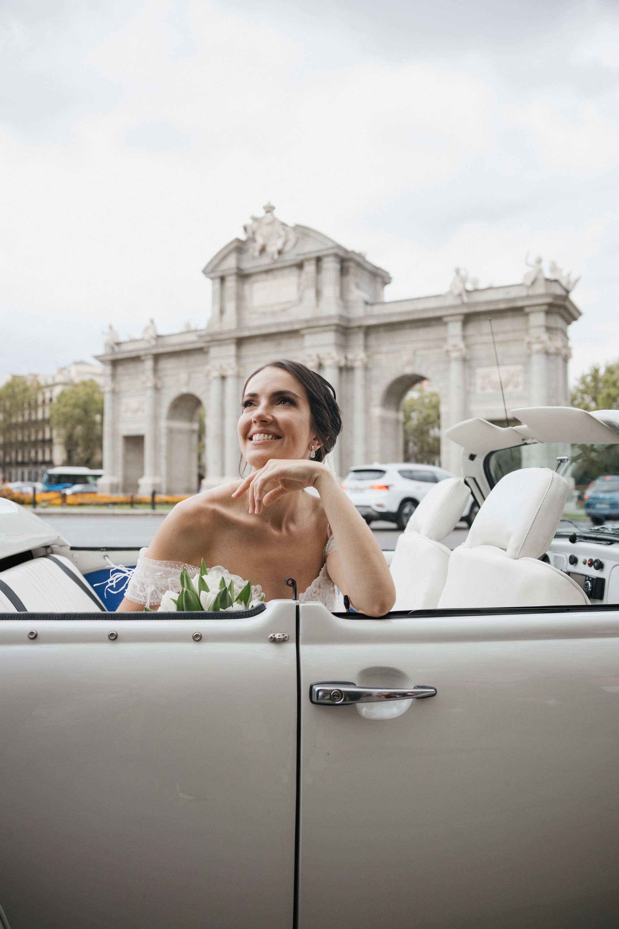 La novia sonríe desde el coche descapotable frente a la Puerta de Alcalá