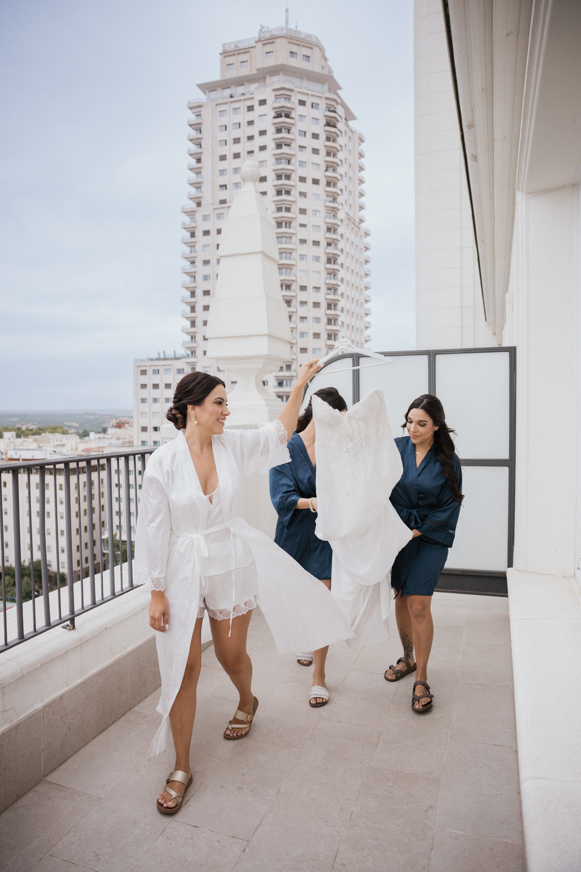 La novia lleva su vestido en la percha por la terraza del hotel acompañada de dos amigas