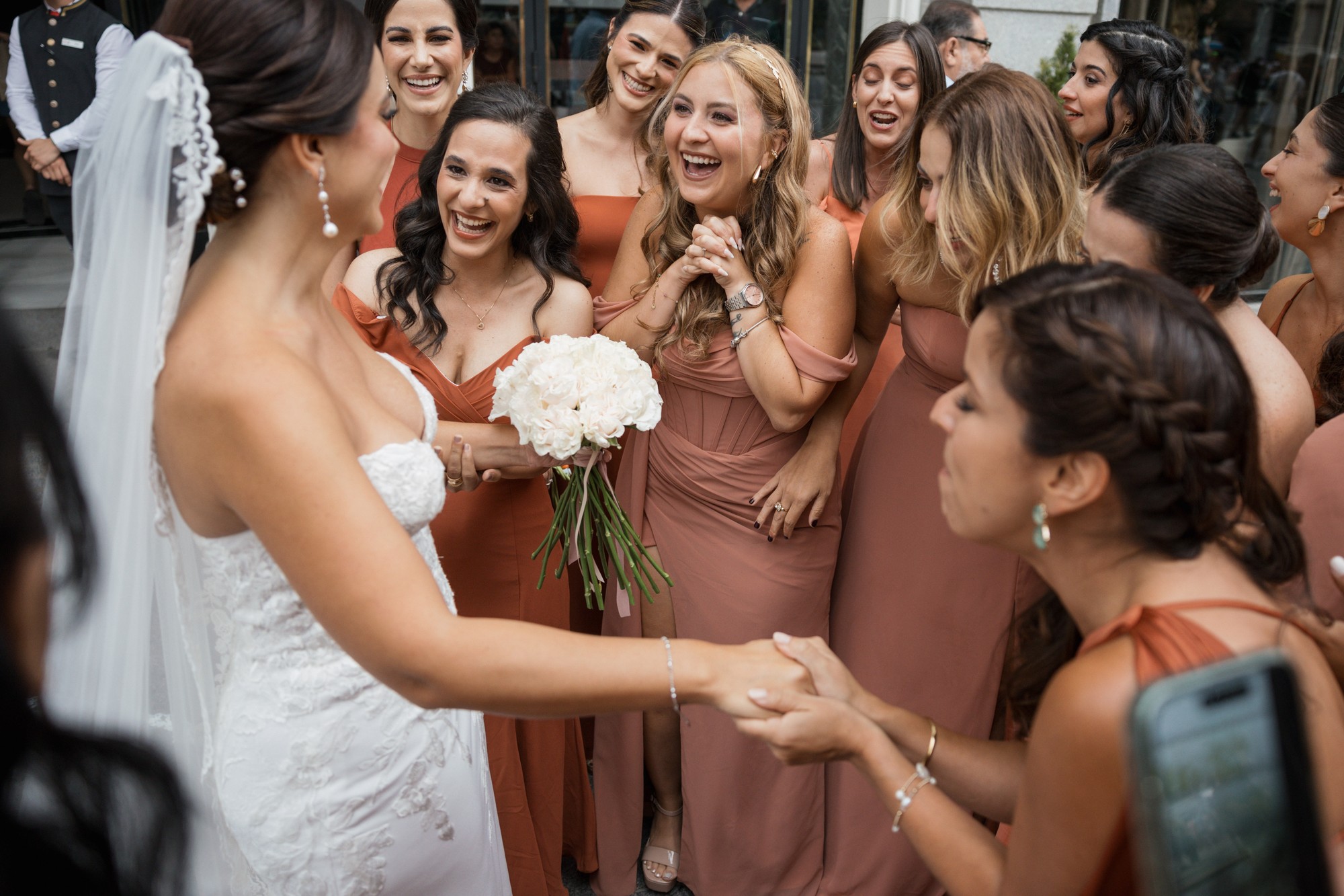 La novia ríe con su ramo de rosas blancas en medio del corro de amigas