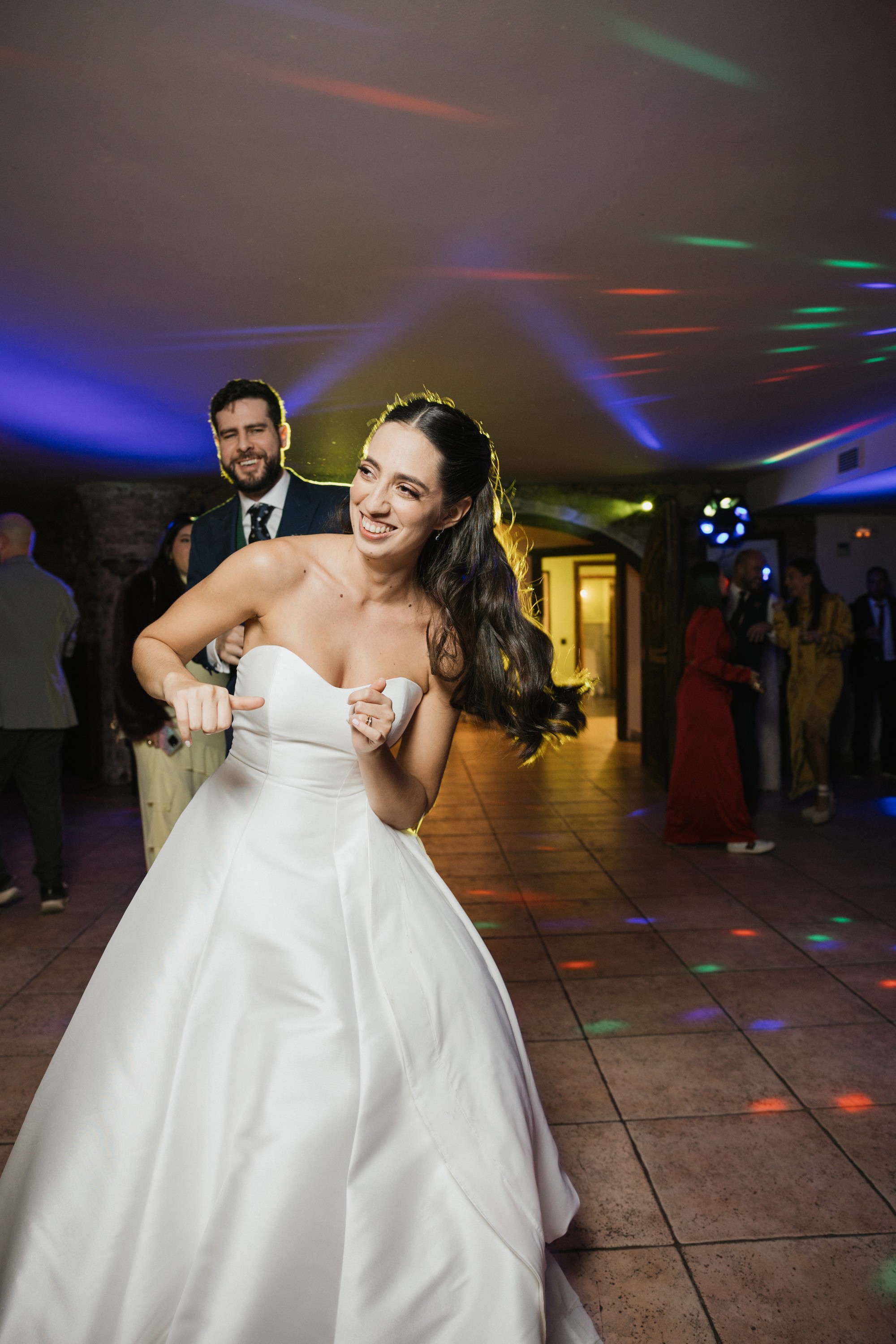 La novia baila con el pelo al vuelo mientras el novio la mira desde atrás