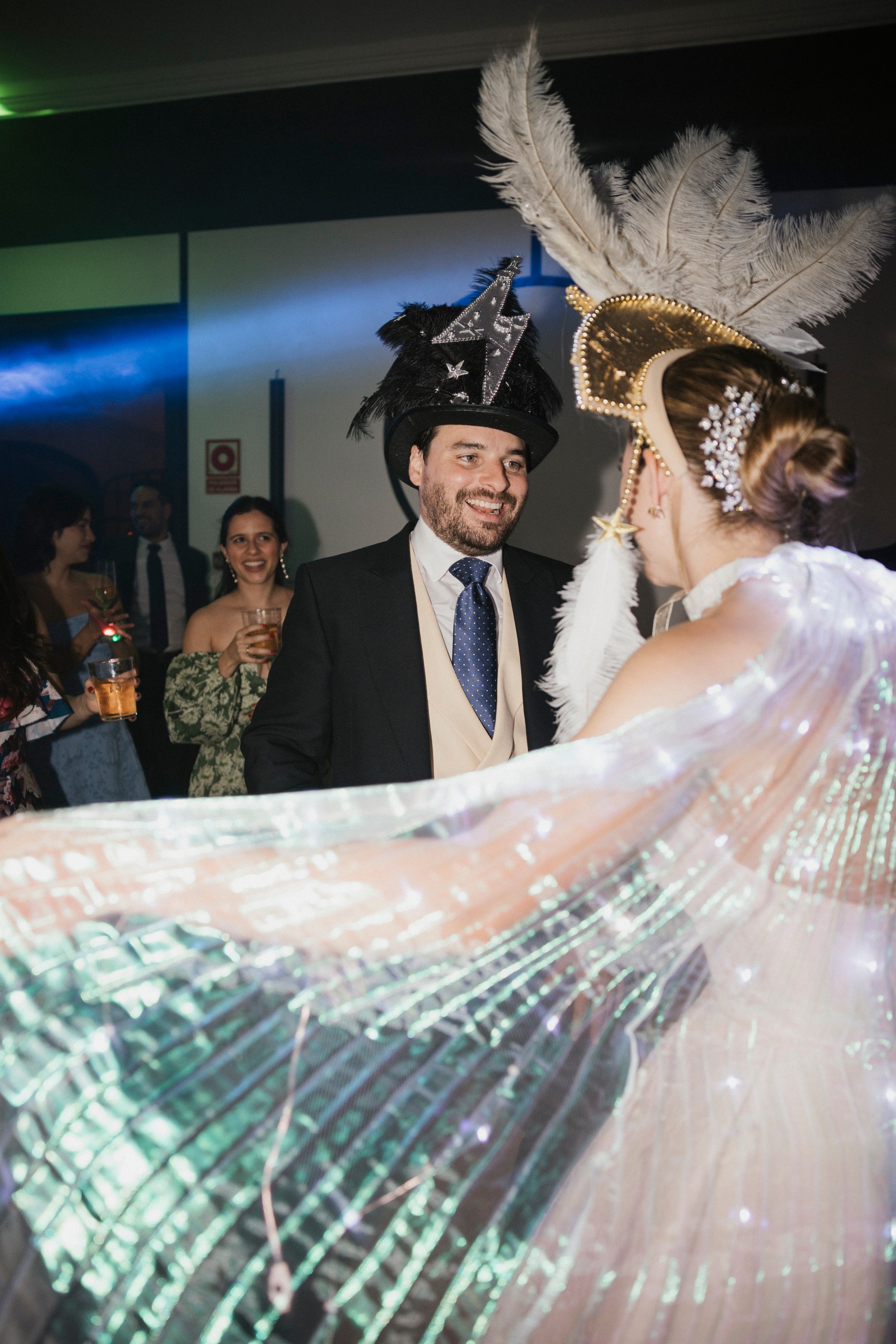 La novia despliega la capa luminosa ante el novio mientras la fiesta sigue