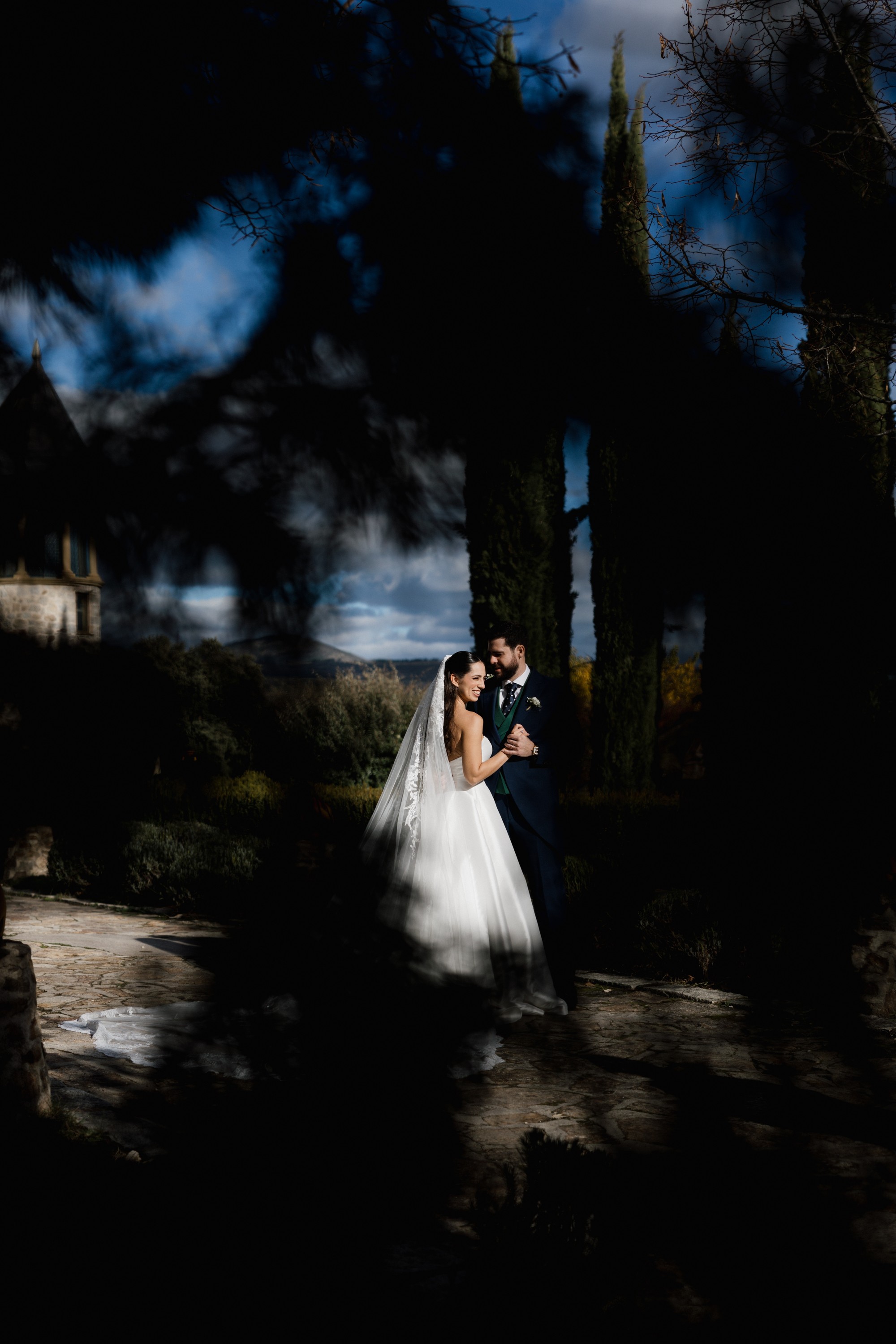 Los novios se abrazan entre cipreses, iluminados por un rayo de sol entre las ramas