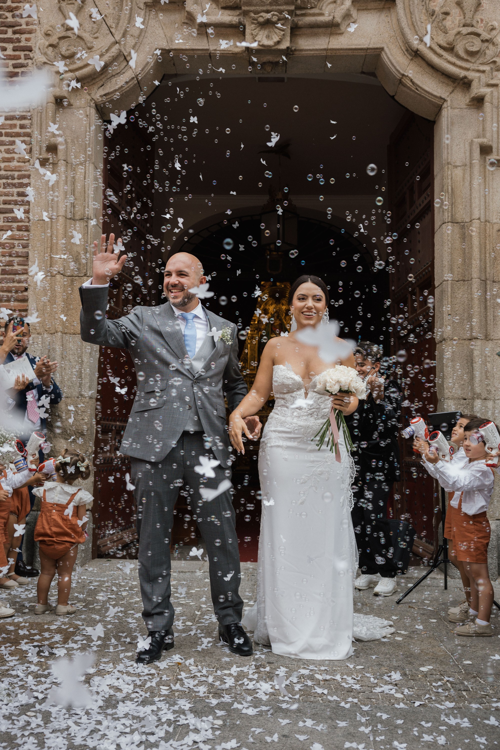 Los novios salen de la iglesia entre burbujas y confeti mientras los niños disparan los cañones