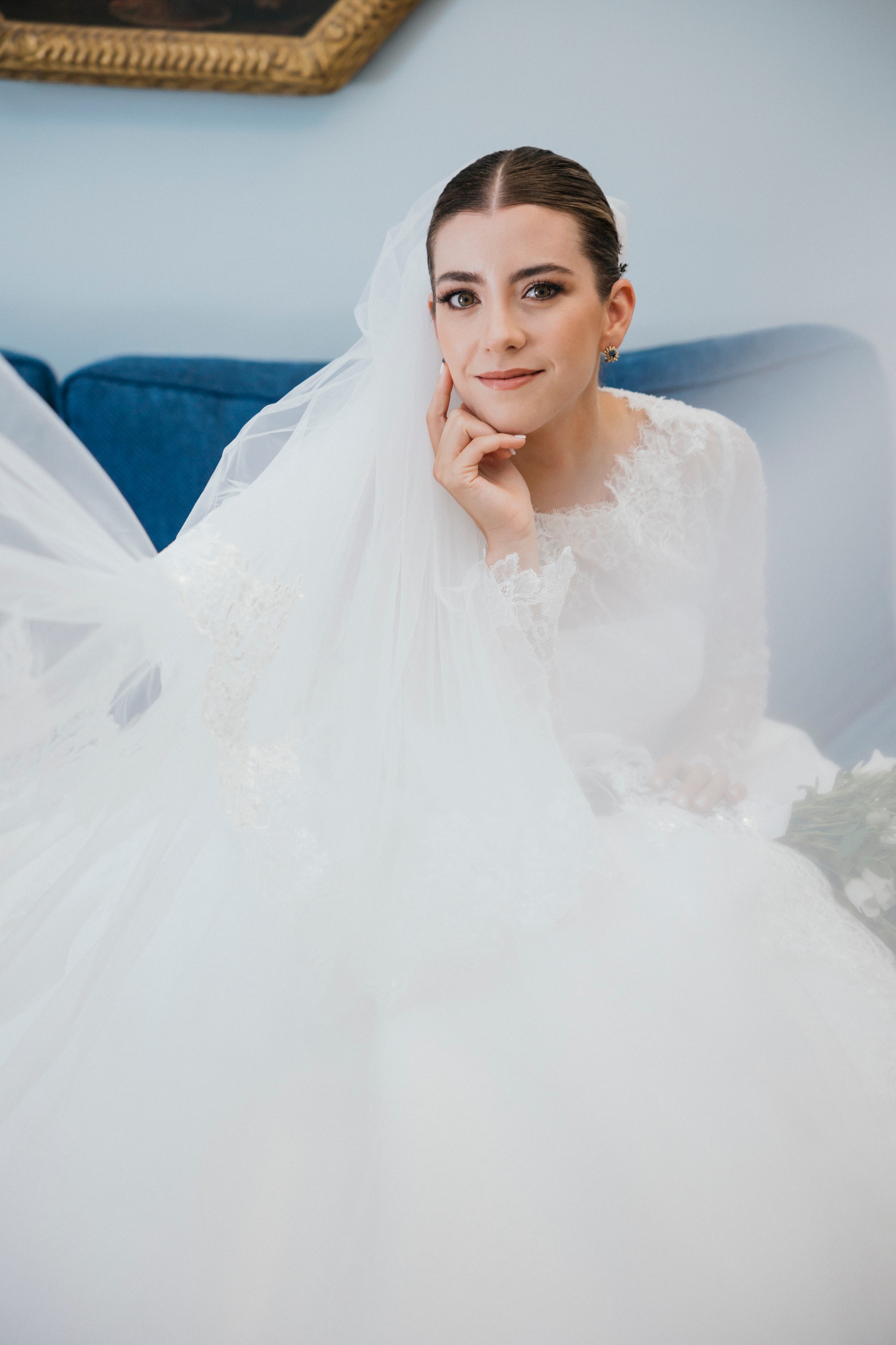 La novia posa con el velo puesto sobre el sofá azul antes de salir de casa