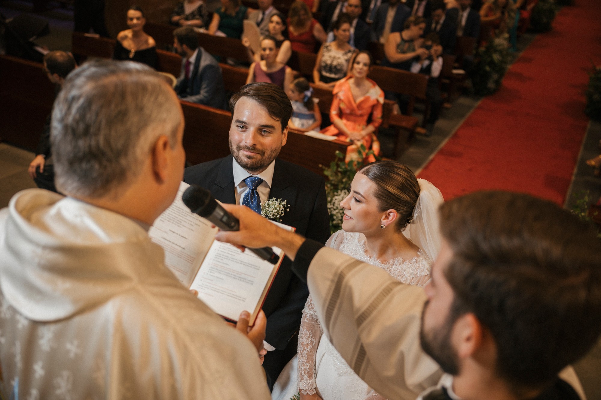 El sacerdote lee en voz alta mientras los novios se miran y escuchan