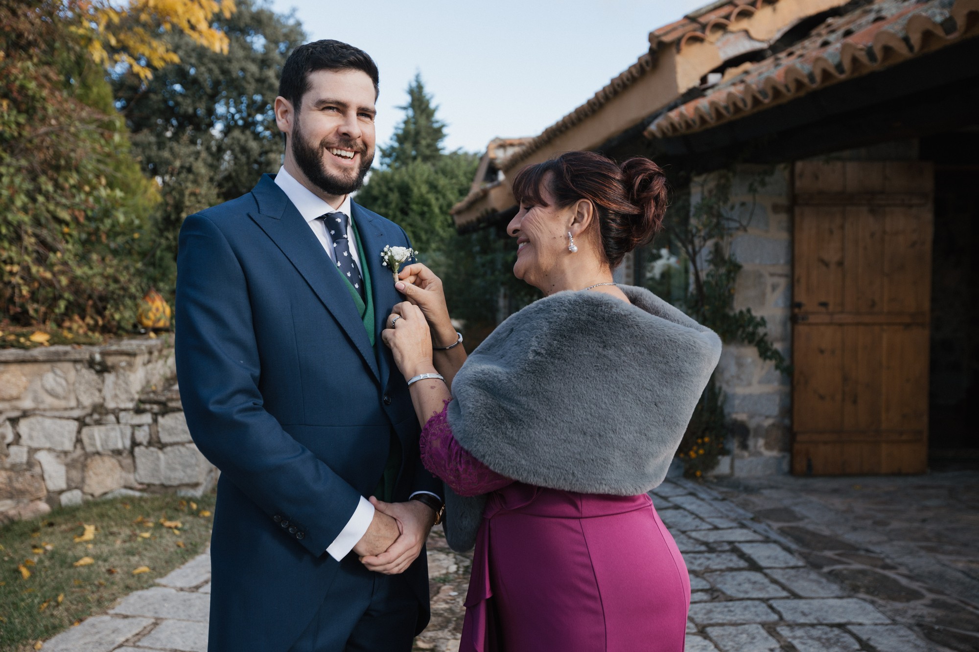 Una invitada coloca el prendido de flores en la solapa del novio a la puerta de la finca