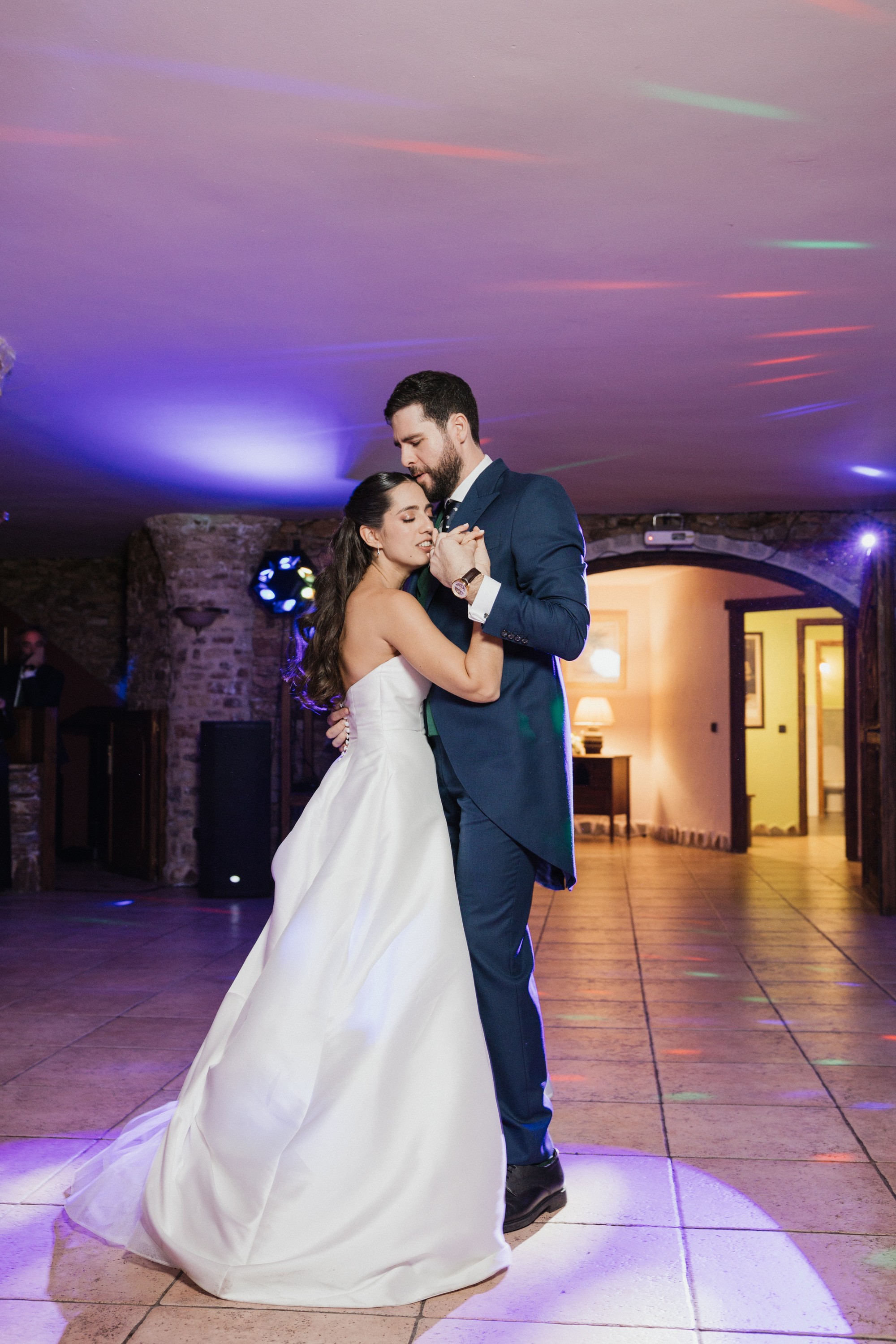 Los novios bailan solos en la pista bajo las luces moradas y él le besa la mano