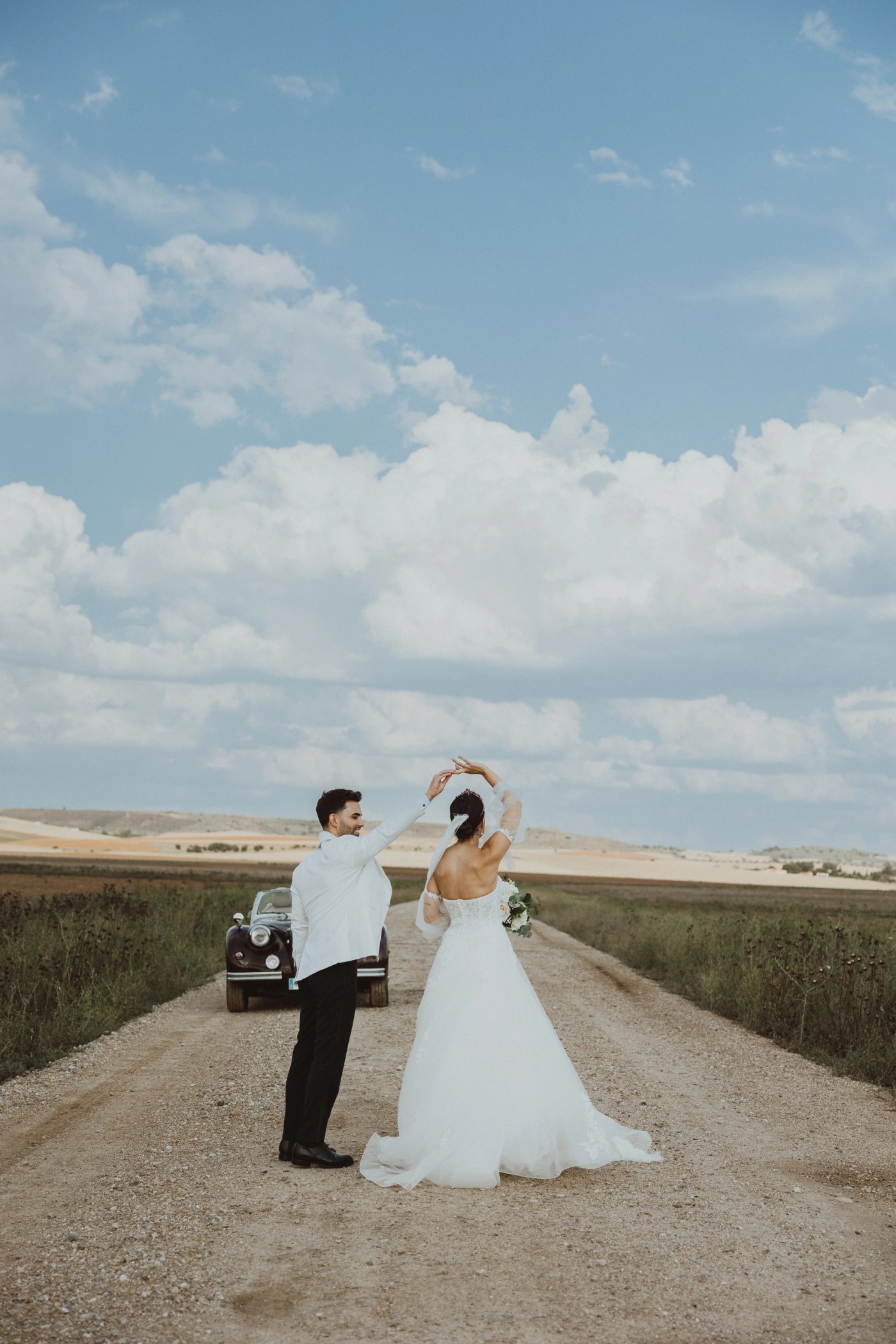 Bride and groom dancing on a country road under a cloudy sky