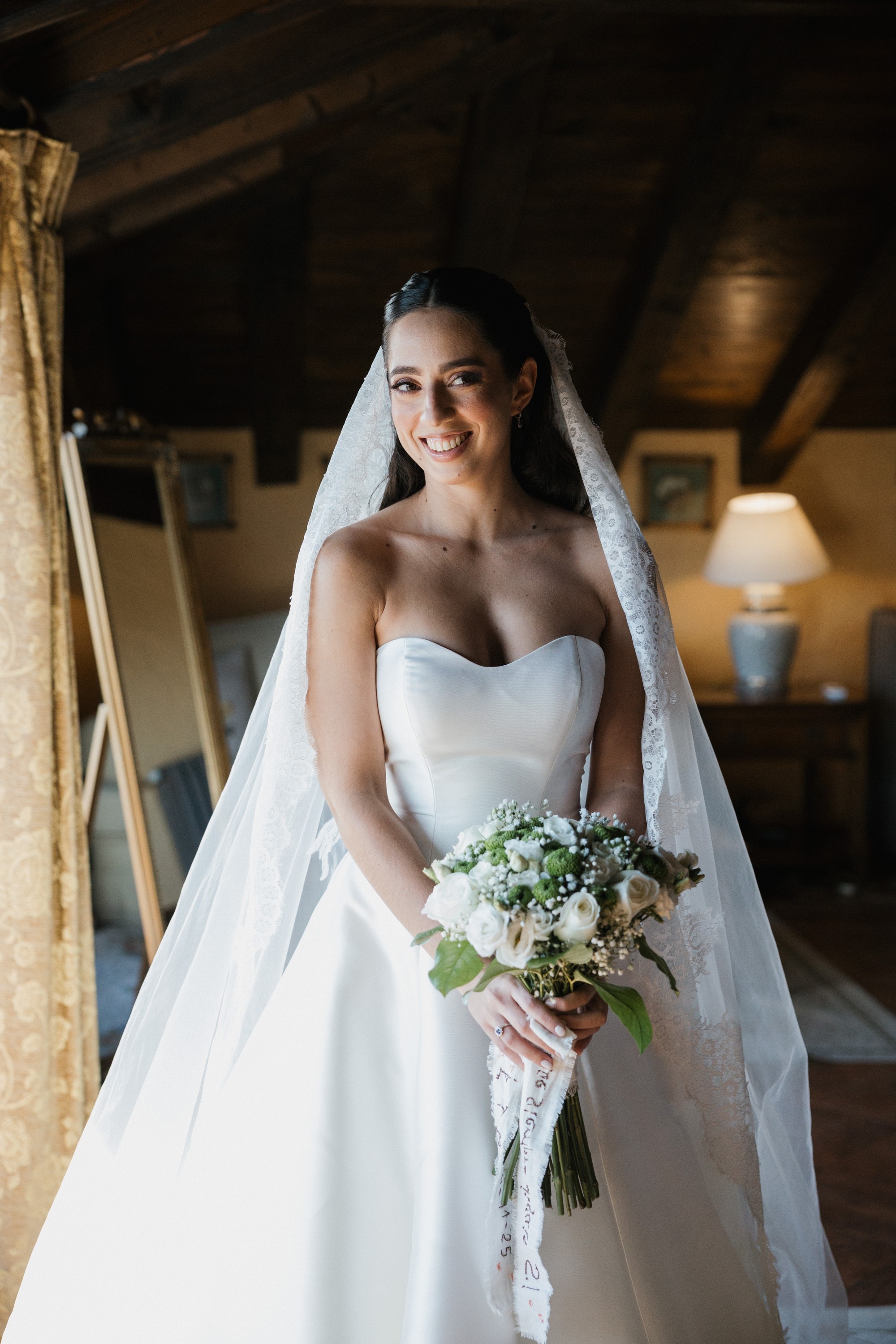 La novia sonríe con el ramo en las manos y el velo de encaje ya colocado