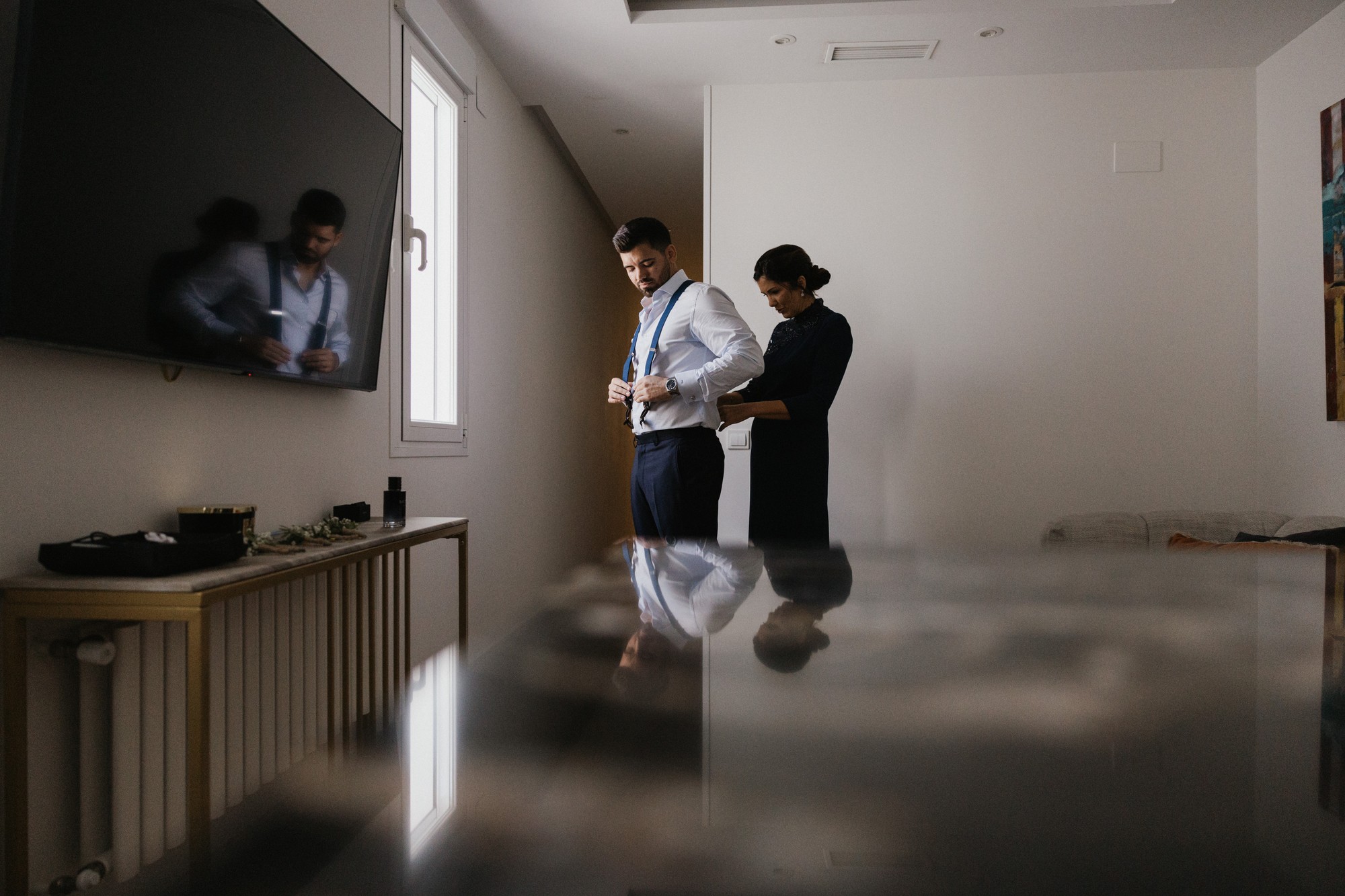 Ajustan los tirantes al novio junto a la ventana durante los preparativos