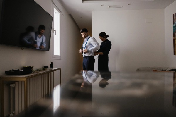 Adjusting the groom's braces by the window while he gets ready