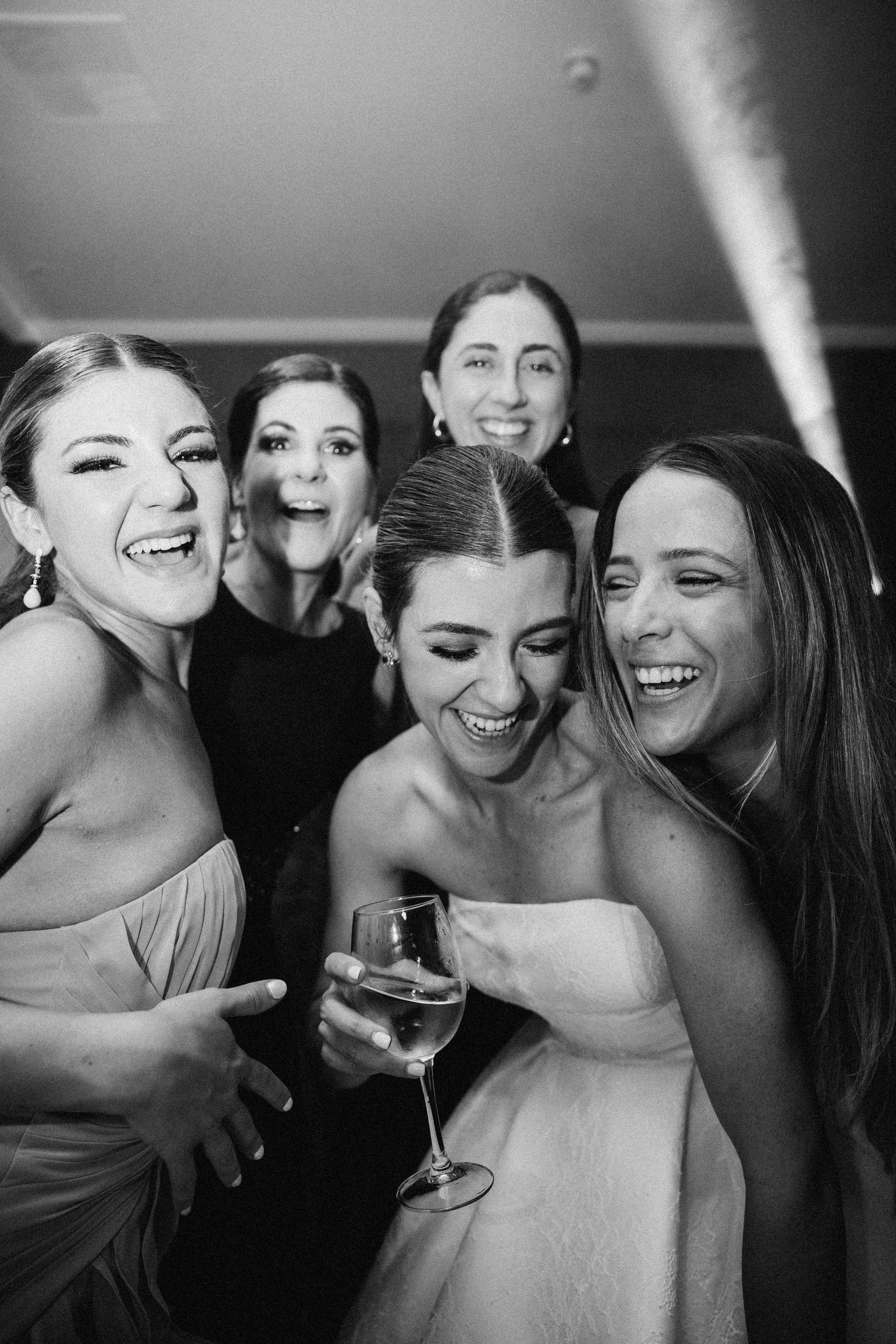 La novia se ríe rodeada de sus amigas con una copa en la mano