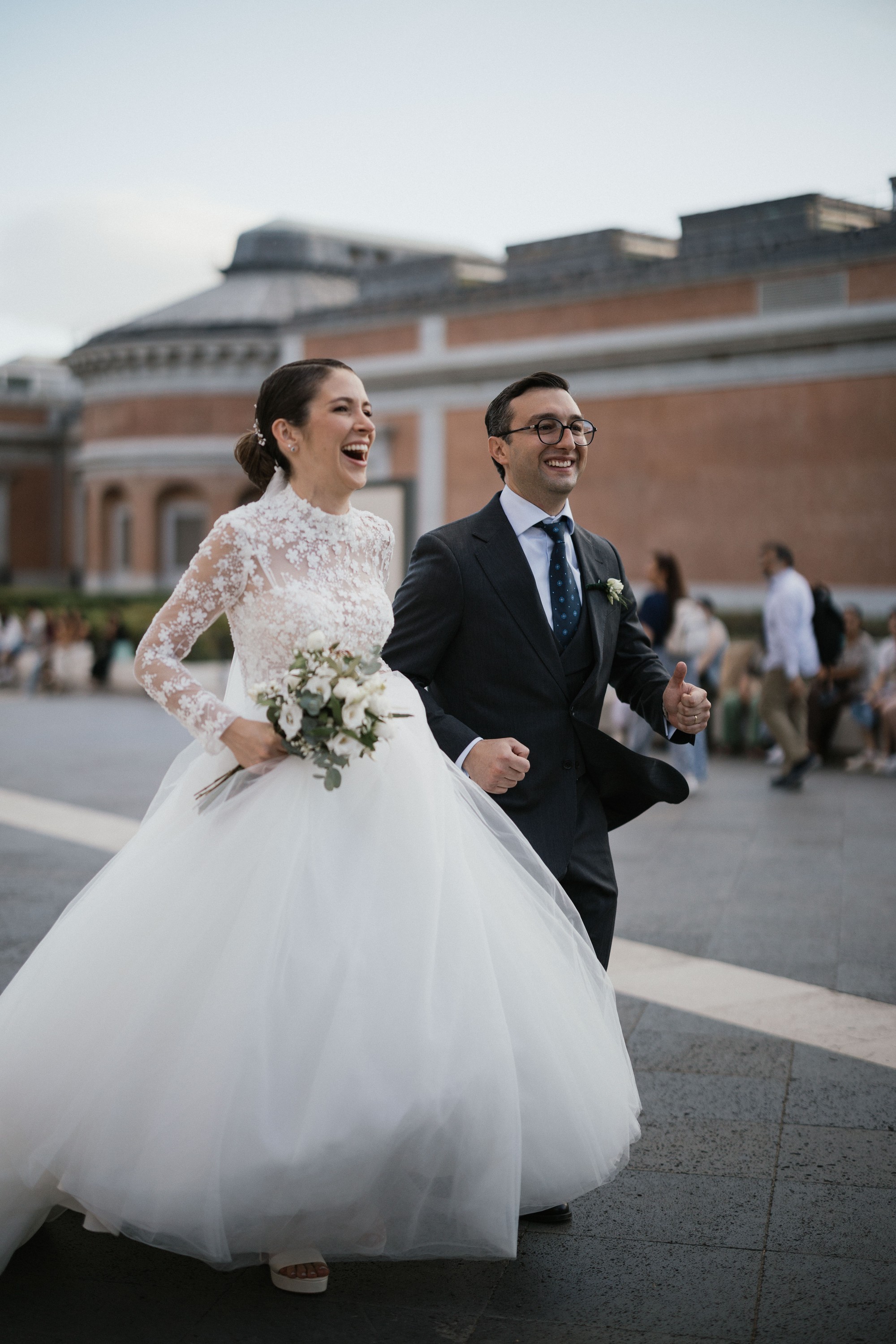 Los novios cruzan riendo una plaza de la ciudad entre los paseantes